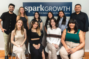 The Spark Growth employees (Akshay, Elissa, Julia, Molly, Saurabh, Madelaine, Maddie, Suzanne and Zahrah) in front of spark growth logo wall.